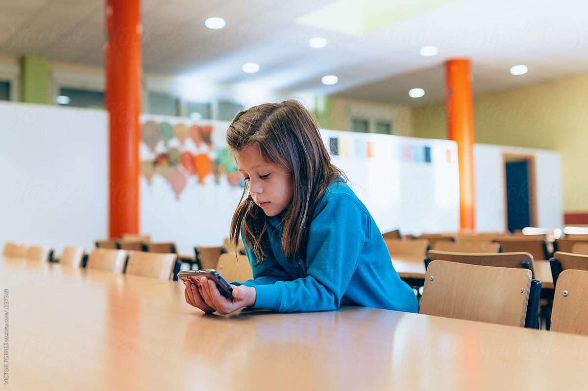 Little girl watching videos on phone in an empty classroom