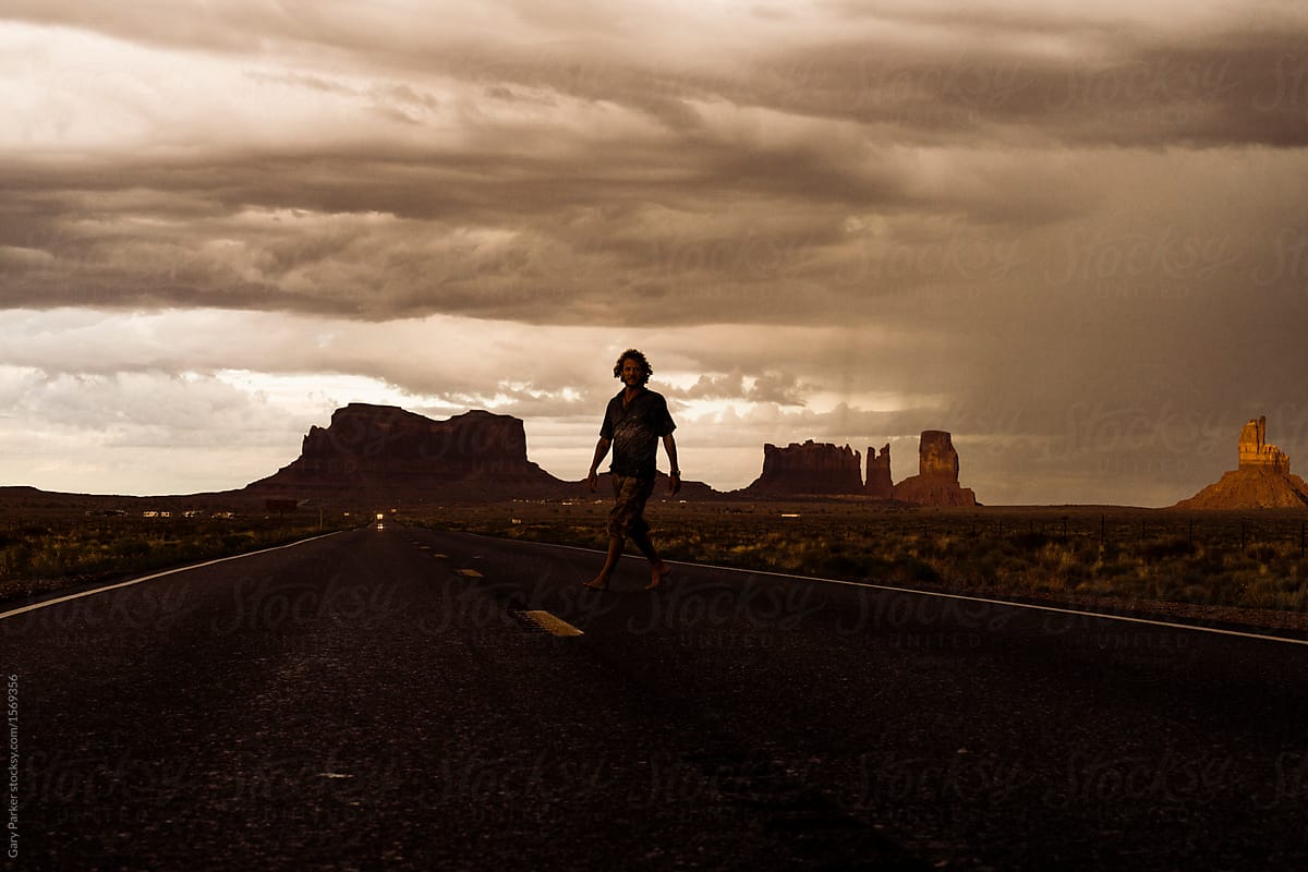 A man walking across a road in front of Monument Valley