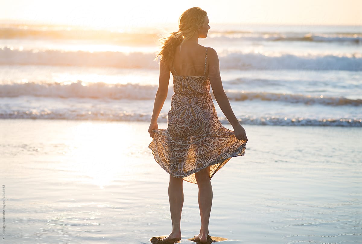 Beautiful young woman standing near the water at the beach as the sunsets.