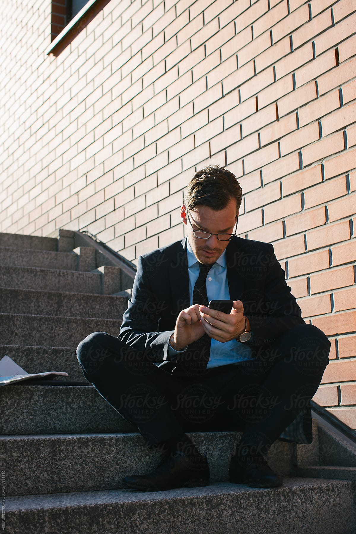 Young Businessman in Blue Suit Sitting on Stairs and Typing on Cellphone