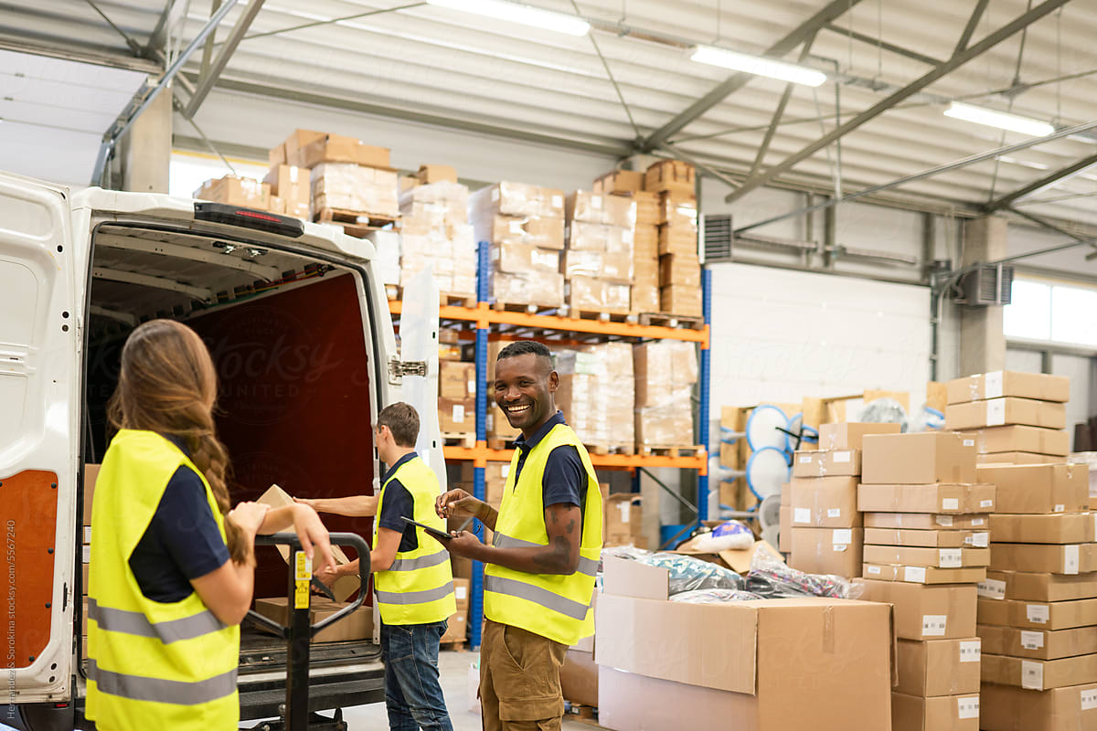 Multiracial Workers Unloading Delivery Van In Warehouse