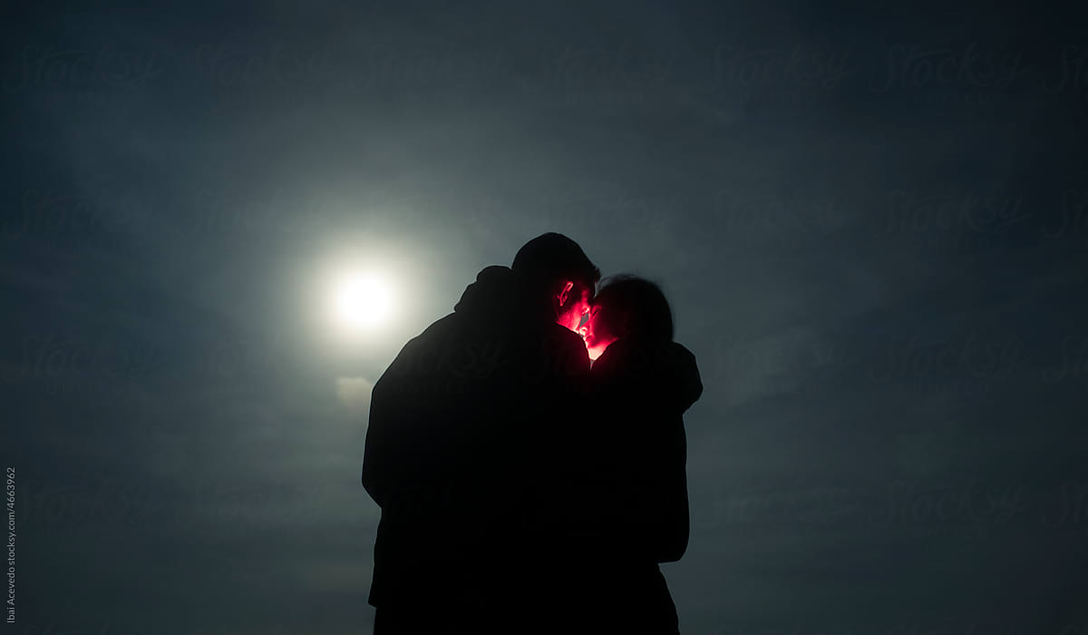 Magical portrait of couple kissing under full moon