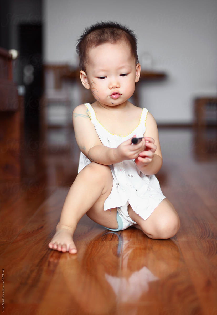 Cute Asian kid playing with paintbrush on the floor at home