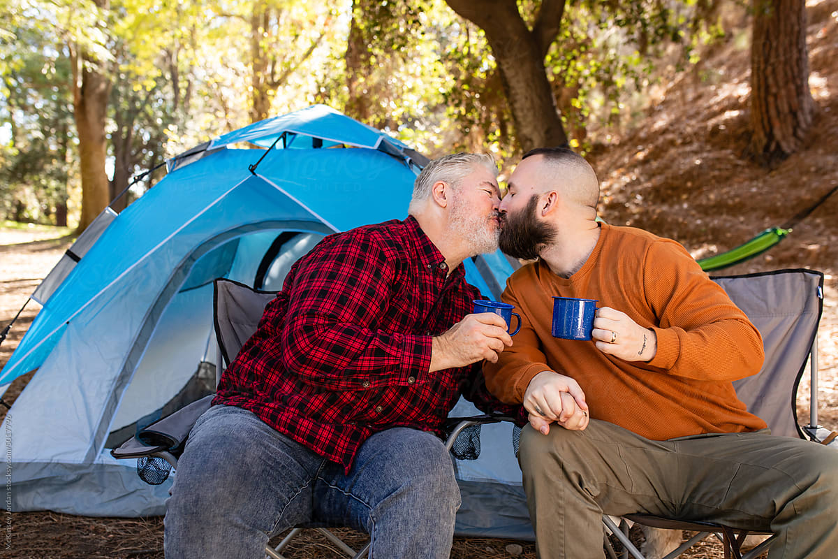 LGBT Couple Hold Blue Mugs And Share A Kiss Outside Of Campsite