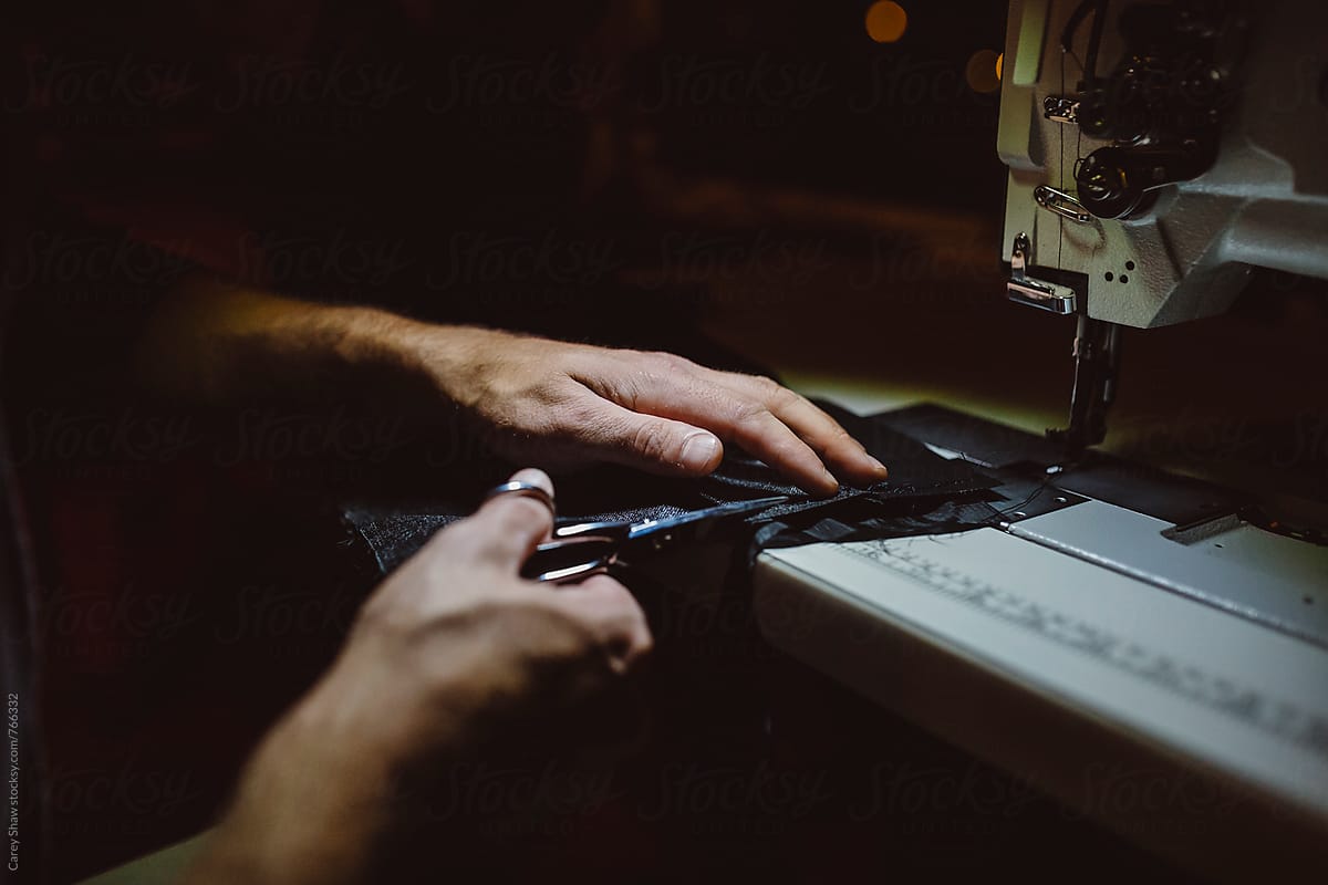  Detail Of Man Cutting Fabric Against Sewing Machine By Stocksy 
