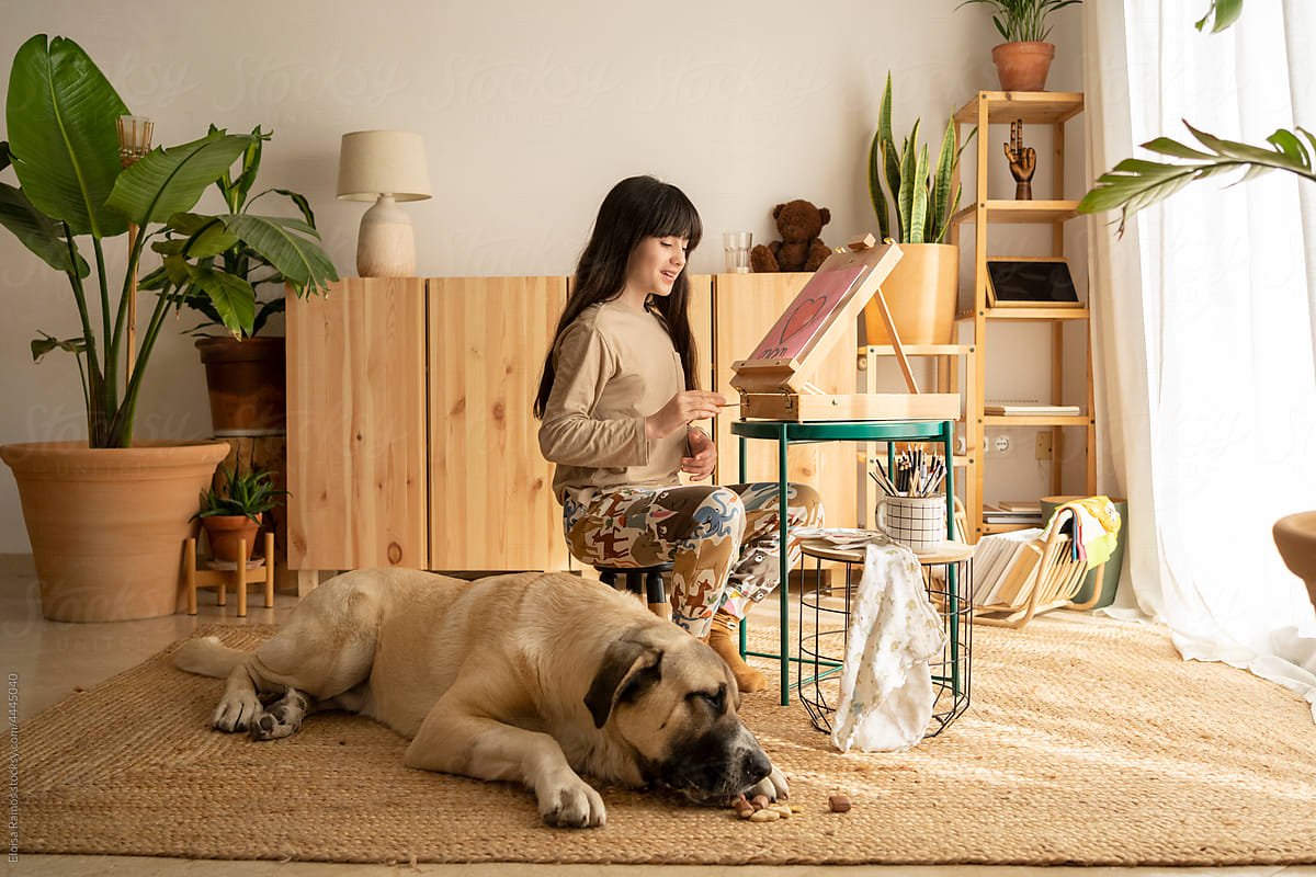 Girl painting picture with her big dog at home