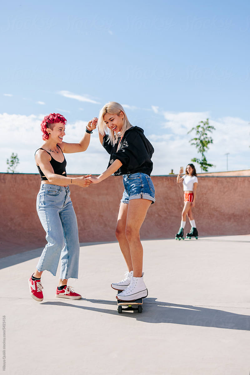 Young girl teaching her friend how to skate. Teenagers having fun.