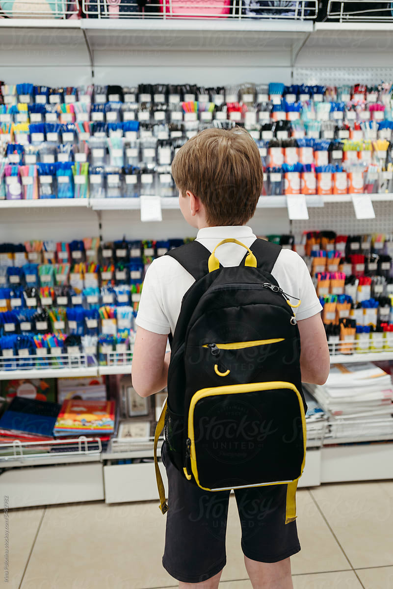 Anonymous schoolboy with backpack chooses stationery in store.