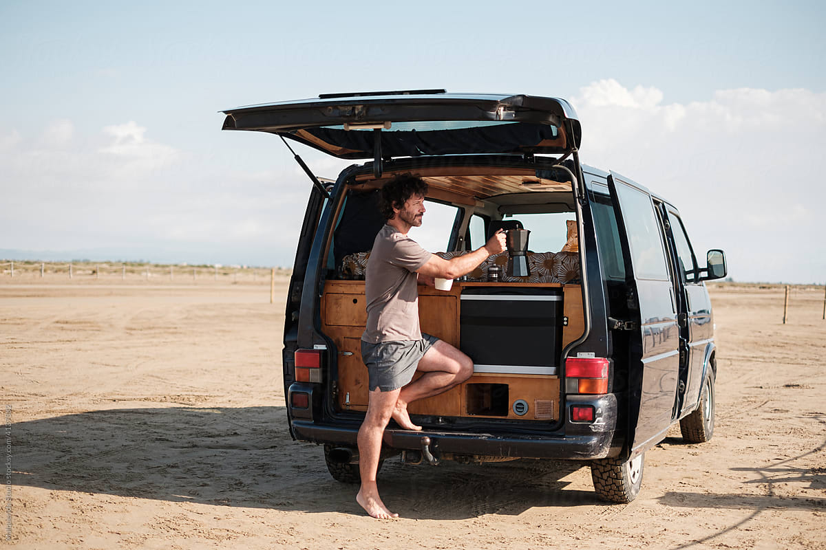 Man preparing coffee in camper van on beach