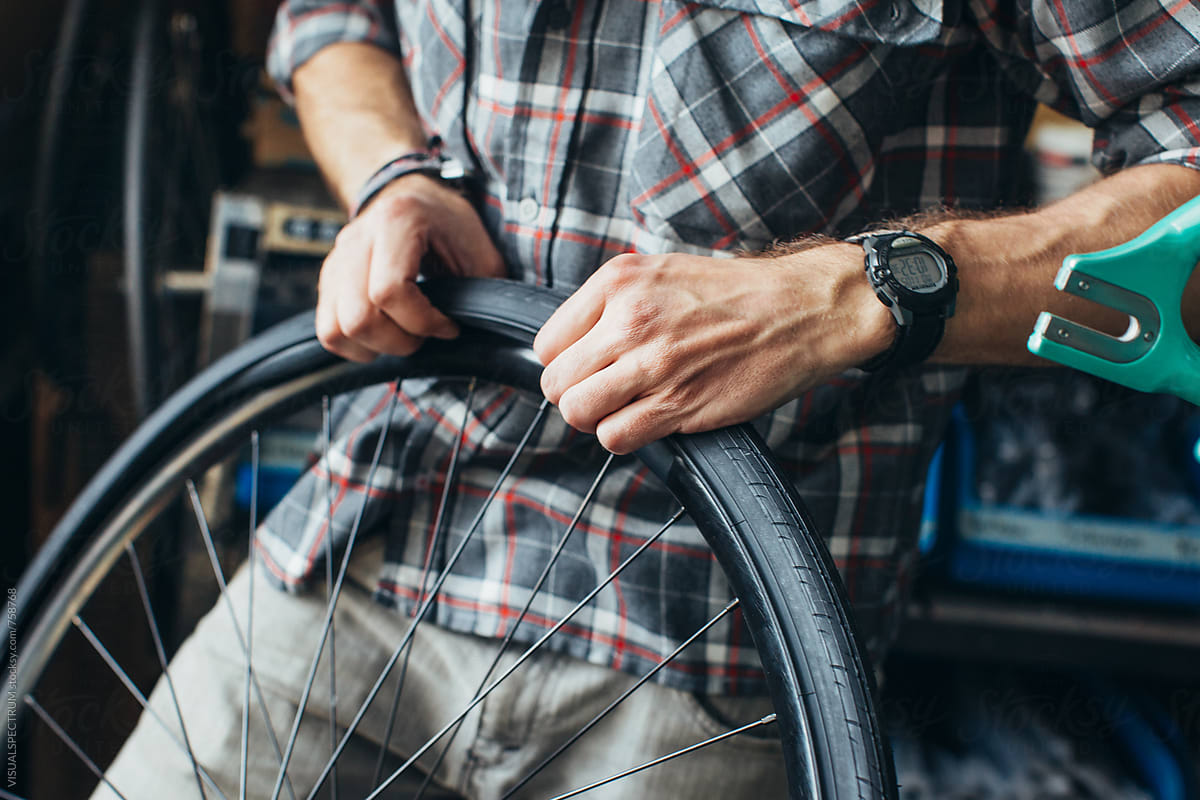 Hands of Young Male Mechanic Assembling Tube and Tire on Bicycle Wheel