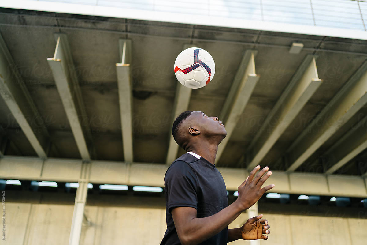 Black sportsman playing football ball on street