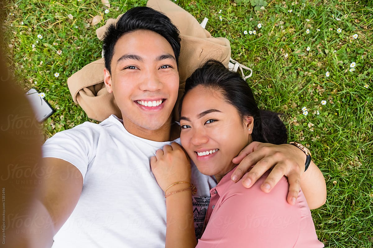 Young Filipino Couple Taking A Selfie While Lying Down On Grass By