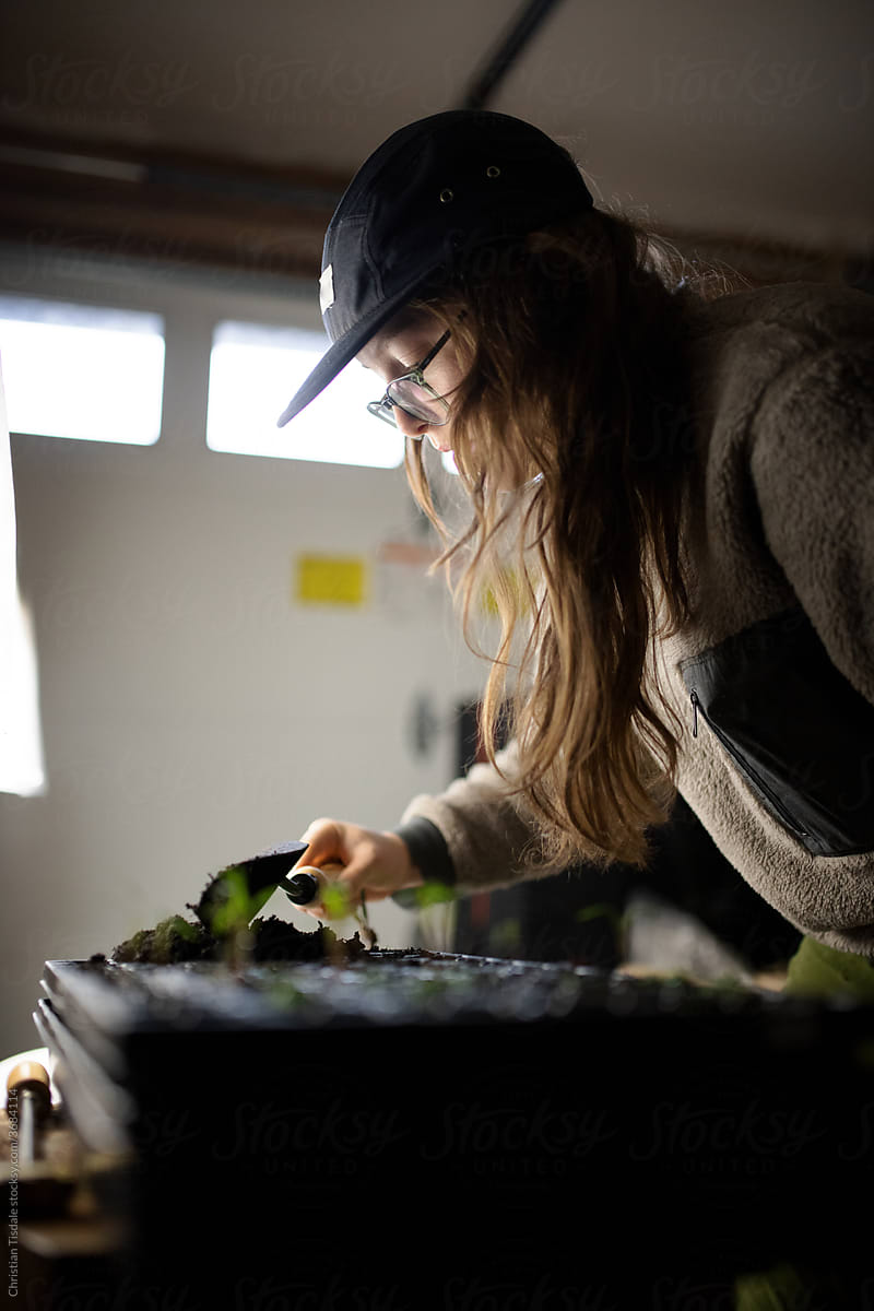 A young woman planting seeds in a plastic container to be grown under lights in a garage