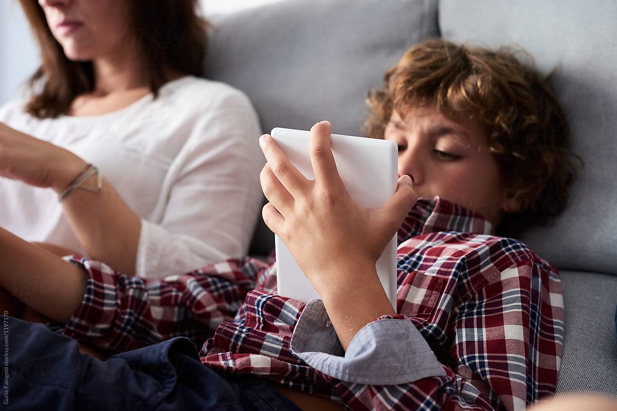 Child in shirt using tablet next to mother