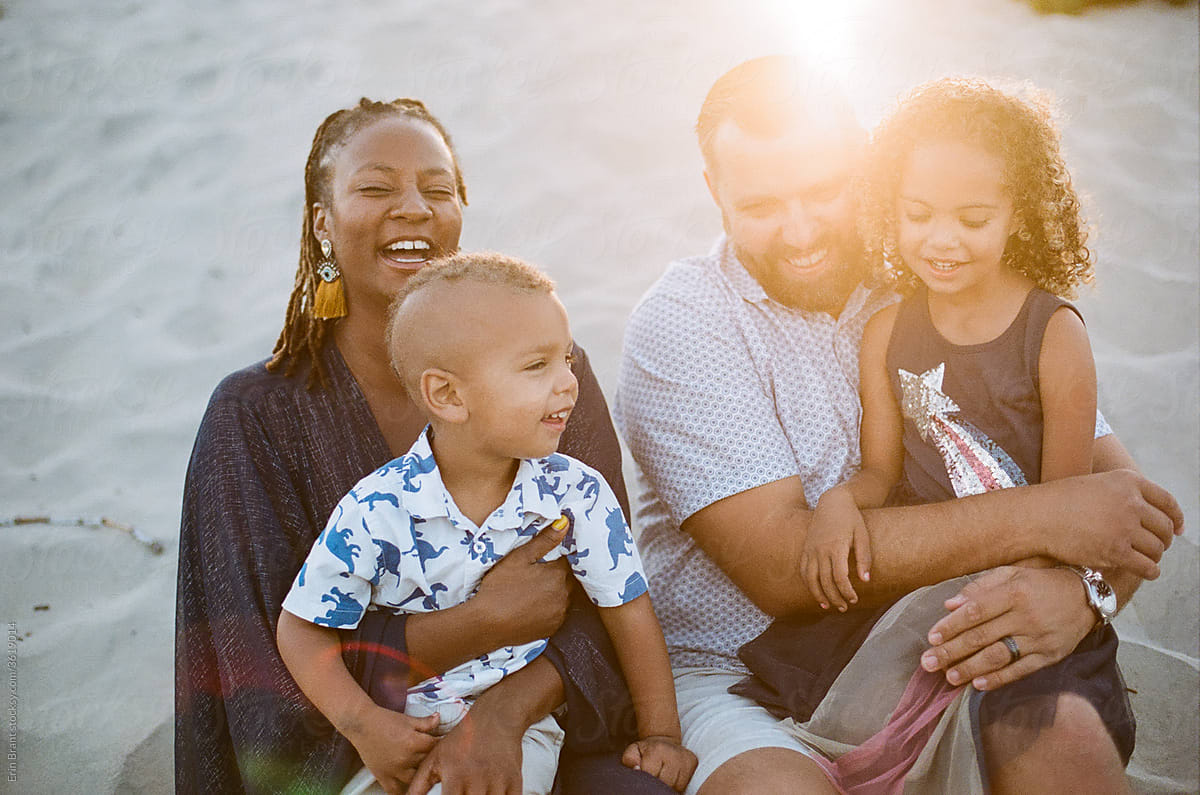Laughing biracial family on beach at sunset