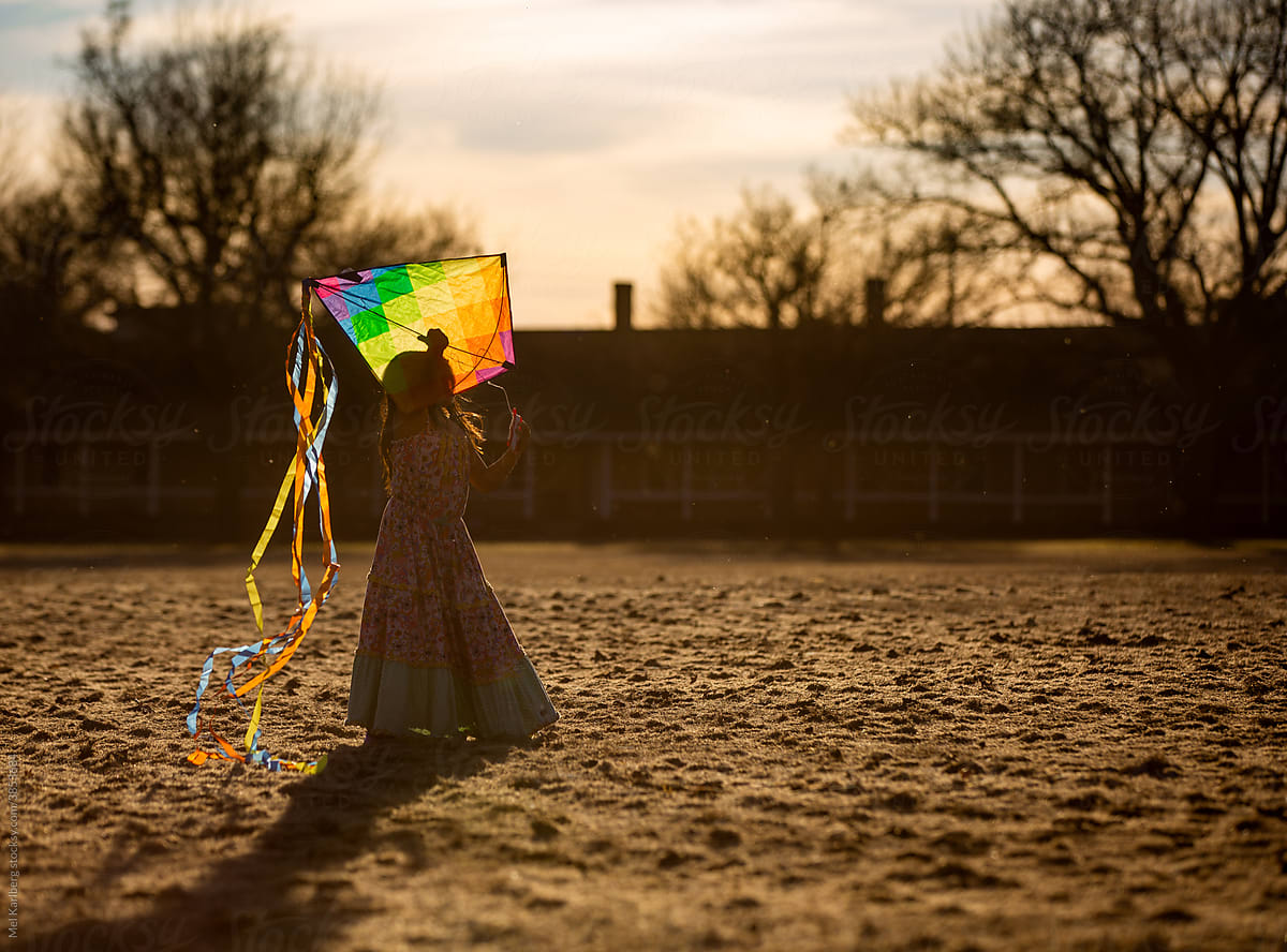 Girl flying rainbow kite at sunset