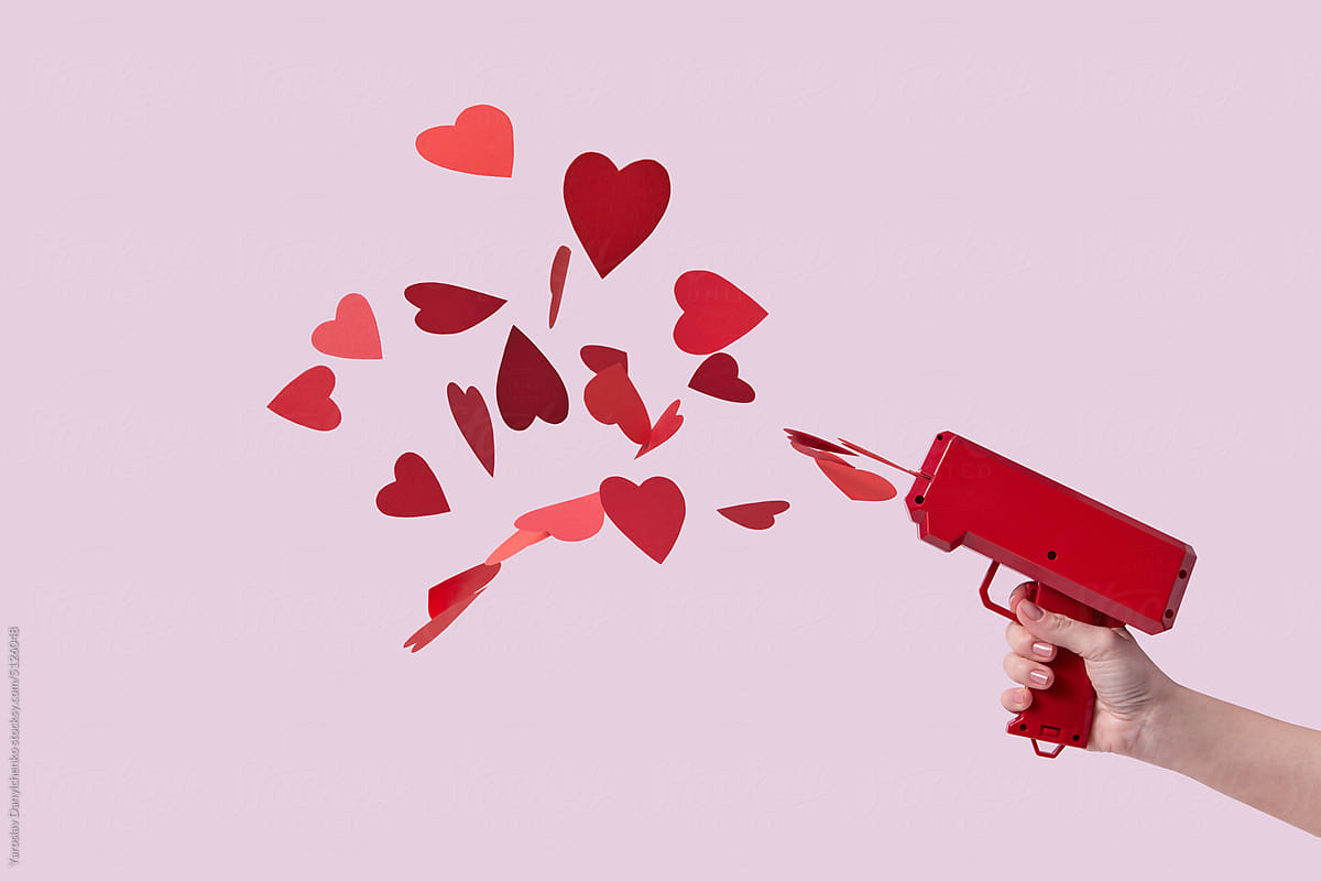 Red hearts flying out of toy gun in woman\'s hand.