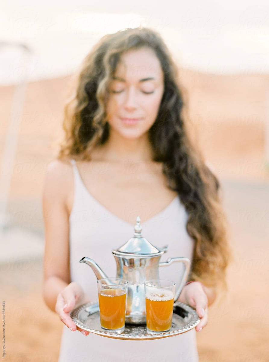 A portrait of a dark-haired woman serving moroccan mint tea in the desert