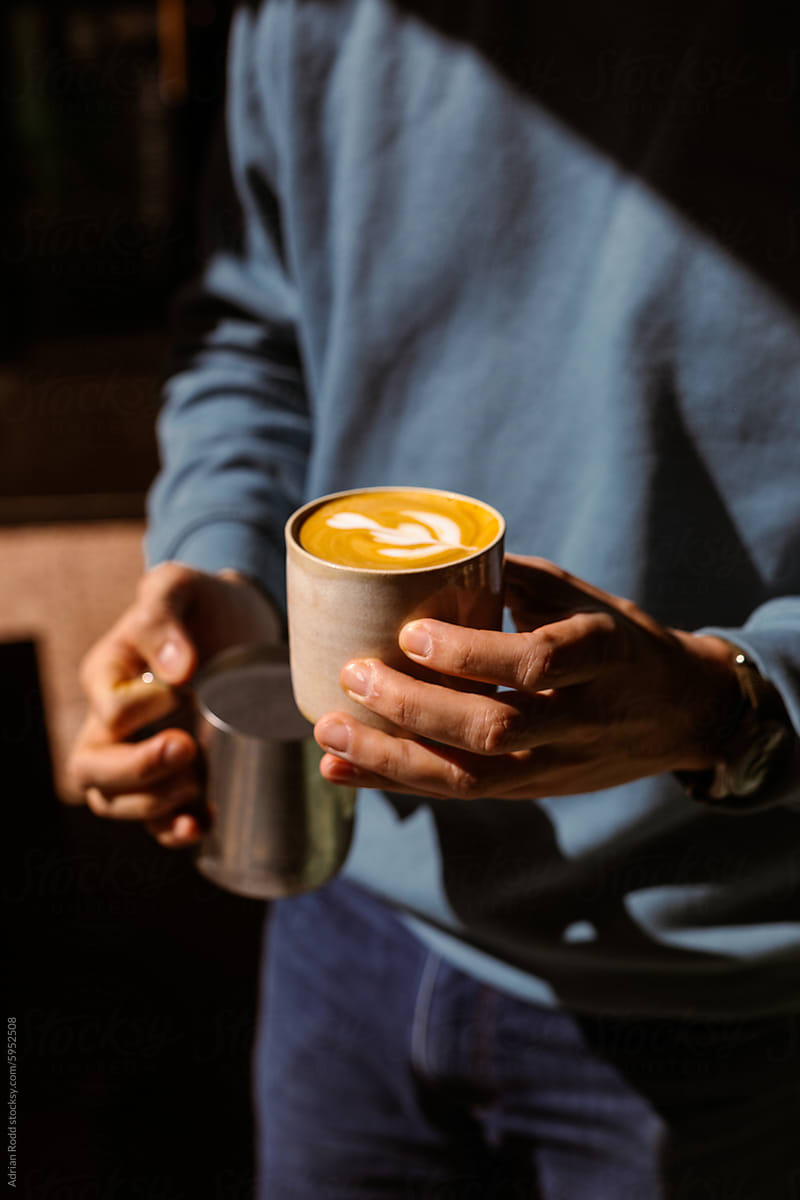 Barista is holding a specialty cappuccino at a fair trade coffee shop