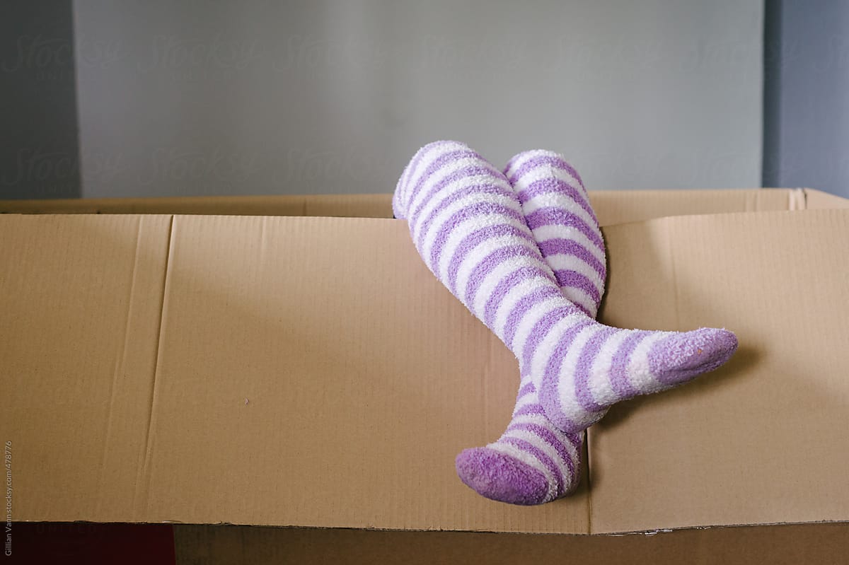 child playing in an empty cardboard box, stripey socks dangling over the side