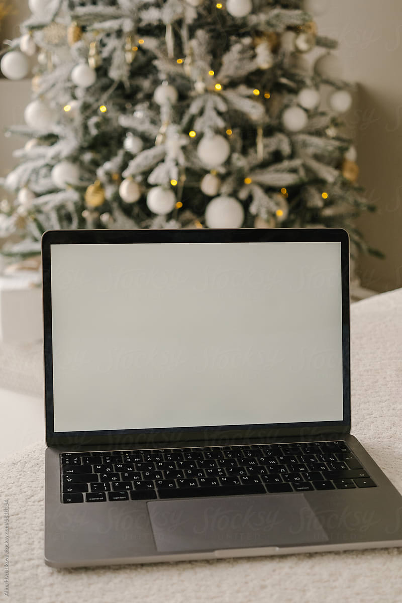 Laptop with blank screen near Christmas tree in room