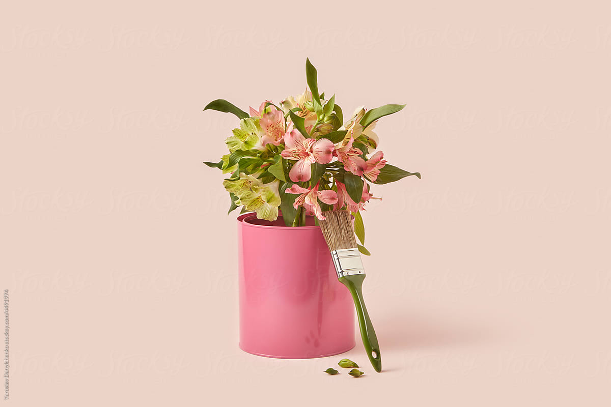 Paint brush leaning on pink tin can with spring flowers