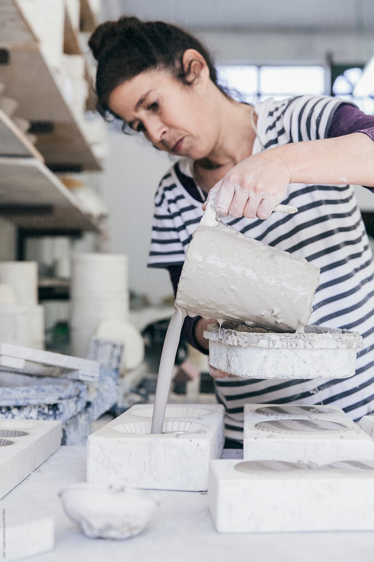 Female ceramic artist pouring wet slip into ceramic moulds
