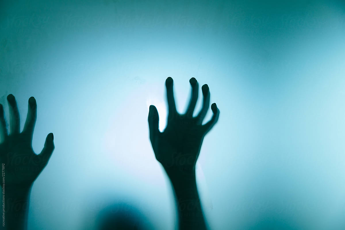 Backlit figure pull their hand against frosted glass.