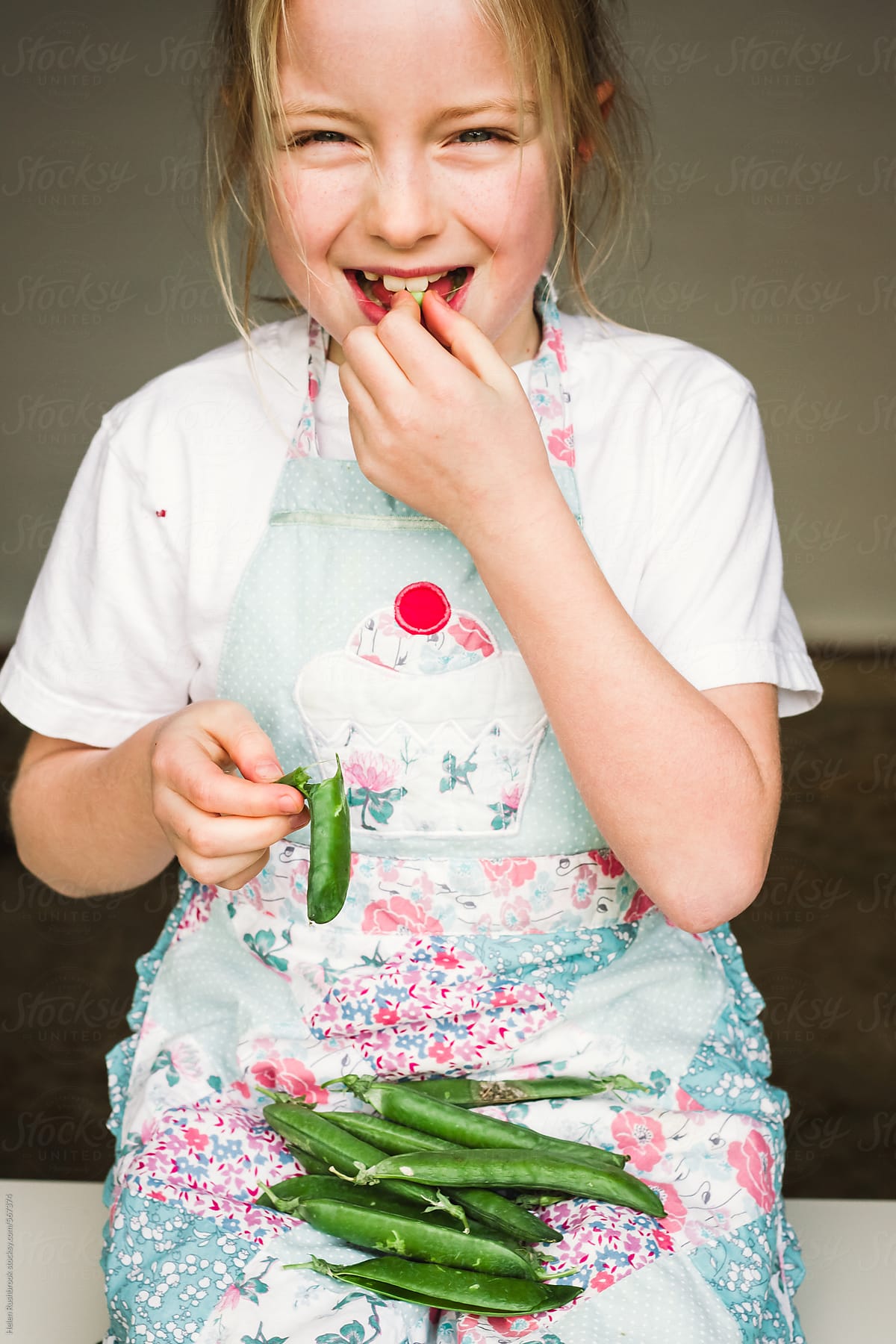 A happy little girl shelling and eating fresh peas.