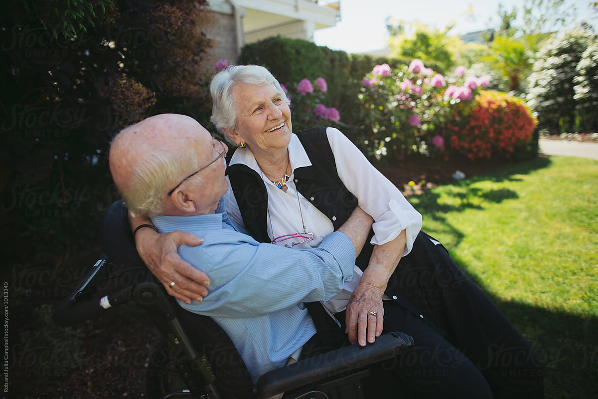 Happy, fun loving elderly couple outside in garden using wheelchair