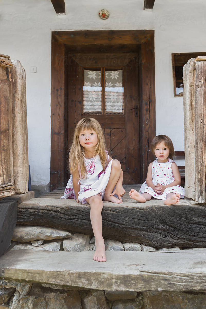 Little girls sitting down on stairs in front of traditional home por