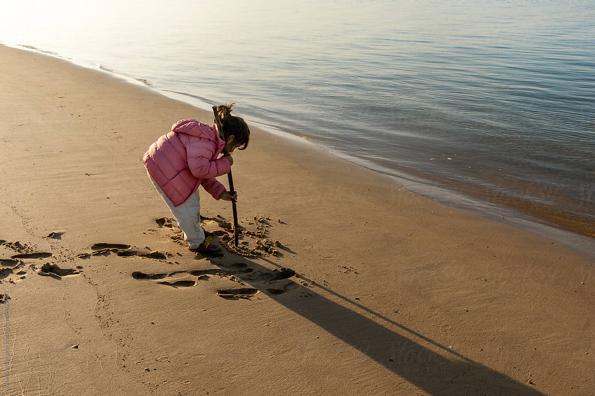 Little girl drawing with stick on the seashore