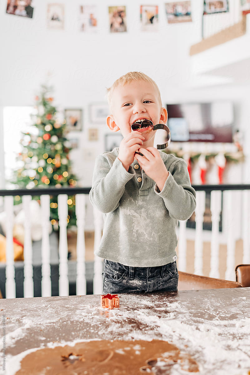 A toddler boy bites gingerbread cookie cutter while baking