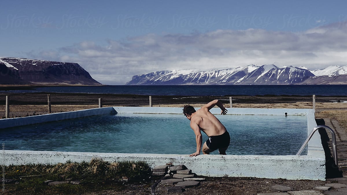 Man in swimsuit jumping into thermal swimming pool outside with snow covered mountains in background