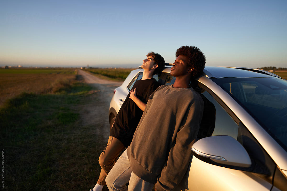 Male friends leaning on car in countryside