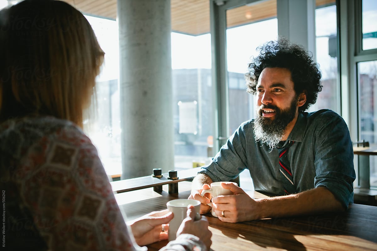 Latin man smiling while chatting with a woman over coffee