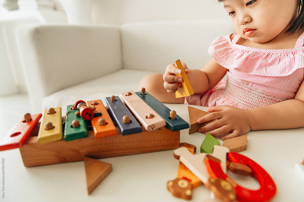 Litle cute child girl plays with colored wooden geometric figures