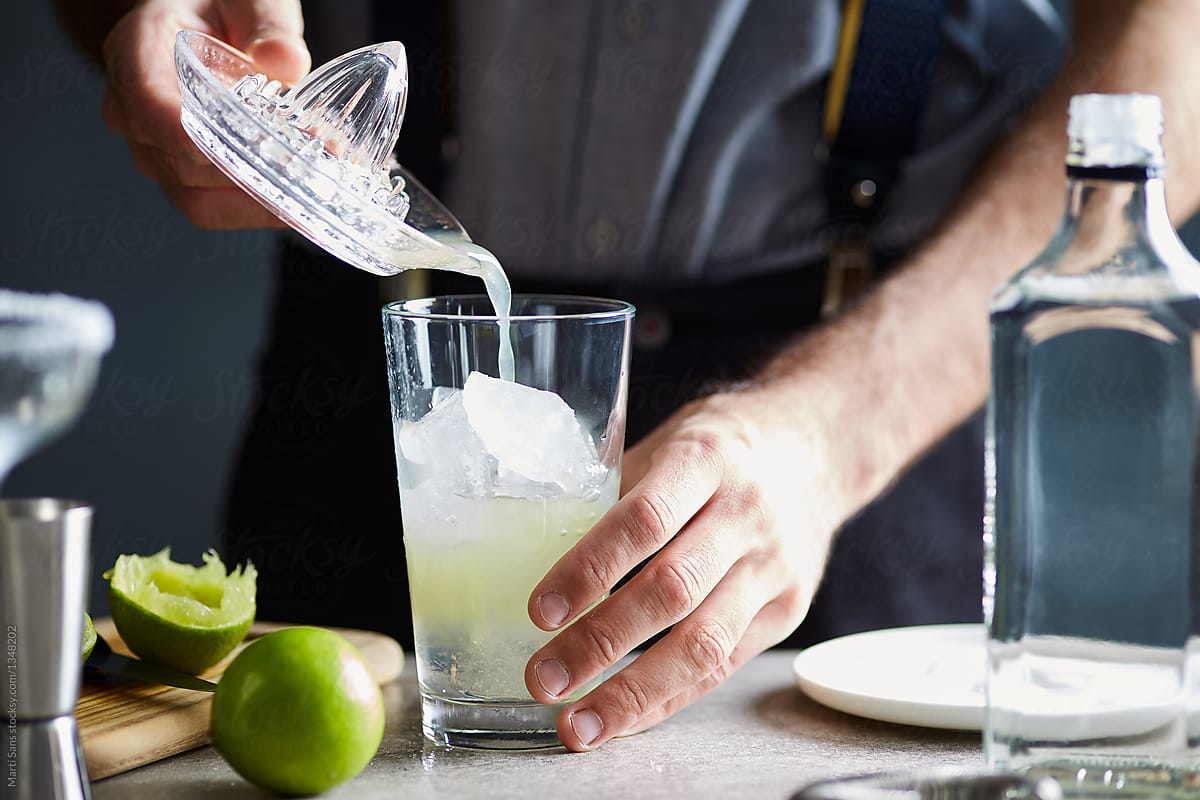 Bartender adding lime juice into glass of ice.