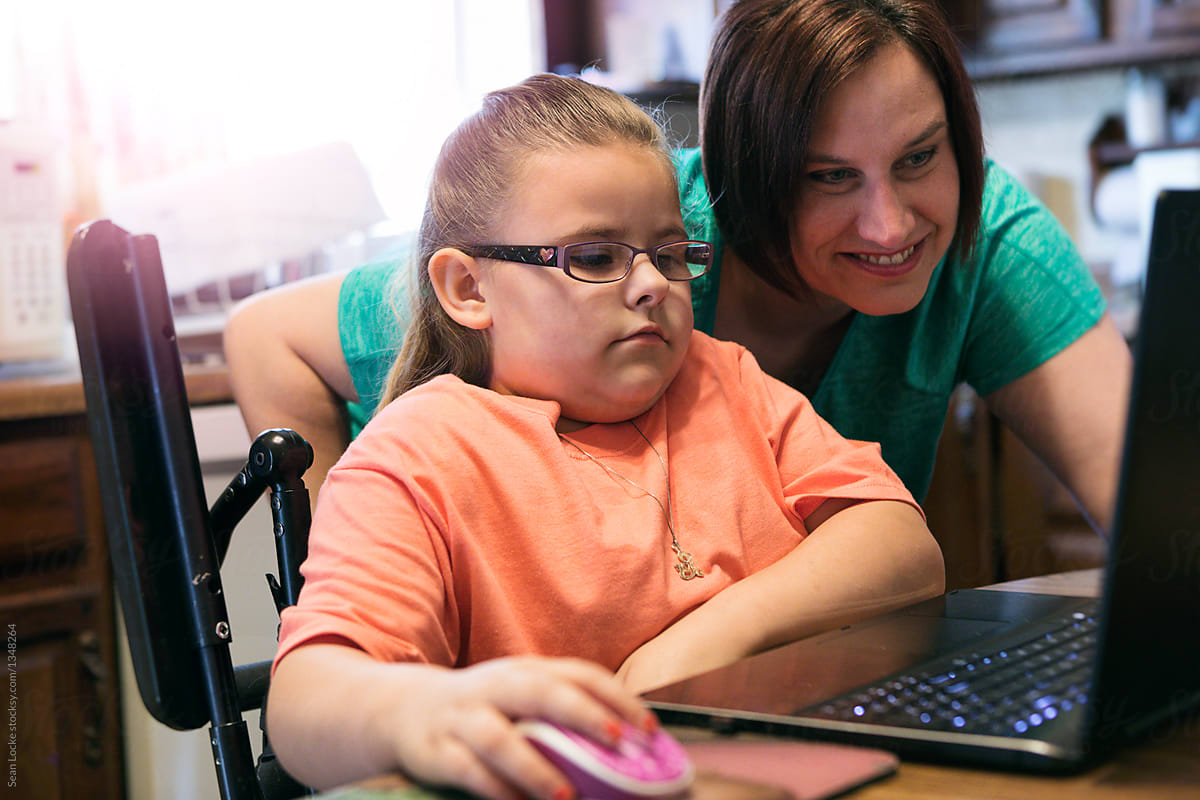 Girl In Wheelchair Uses Laptop With Parental Supervision