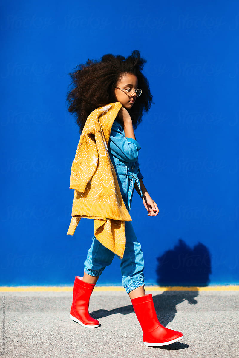 Stylish black girl in rubber boots walking along street