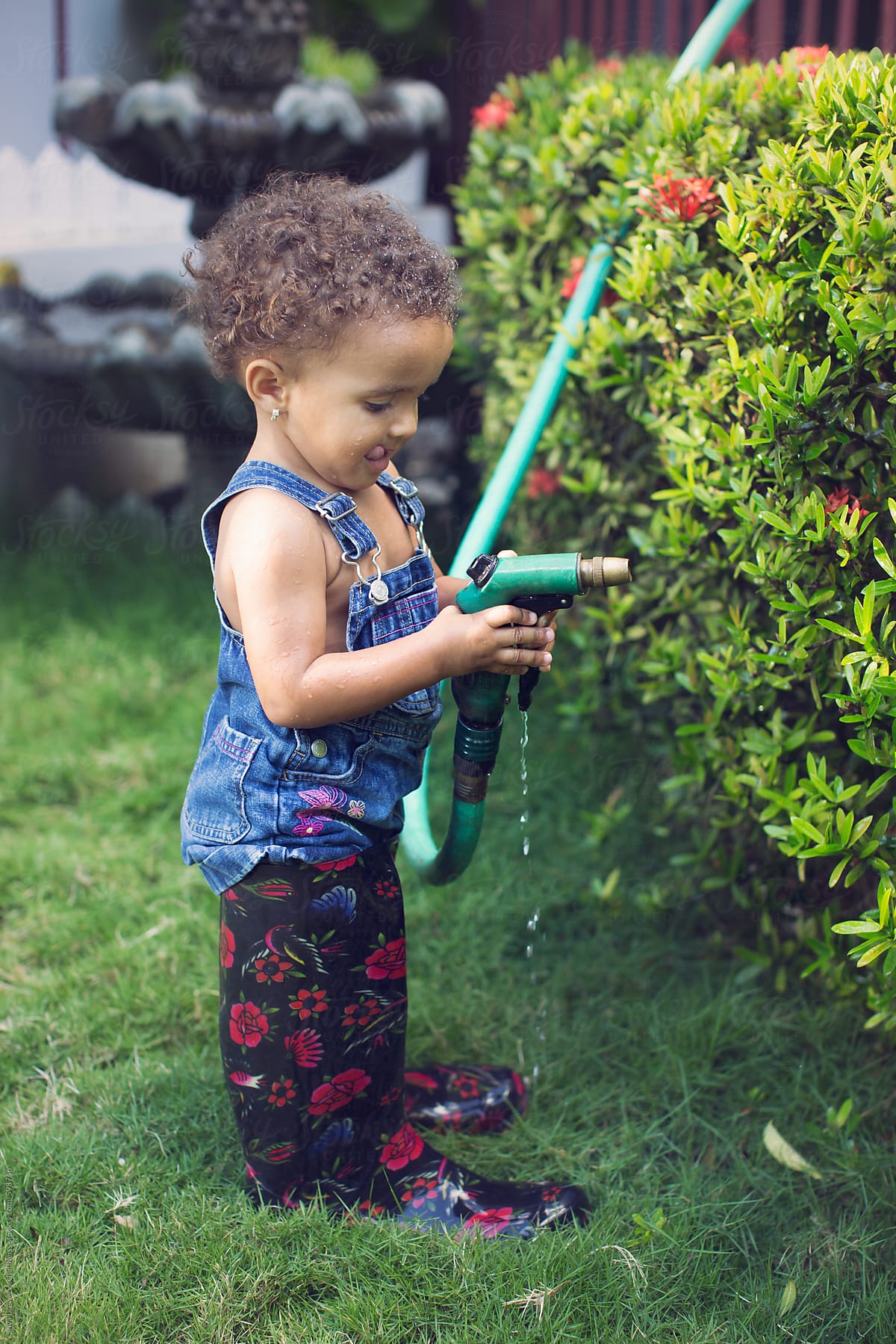A  toddler child playing with a garden hose