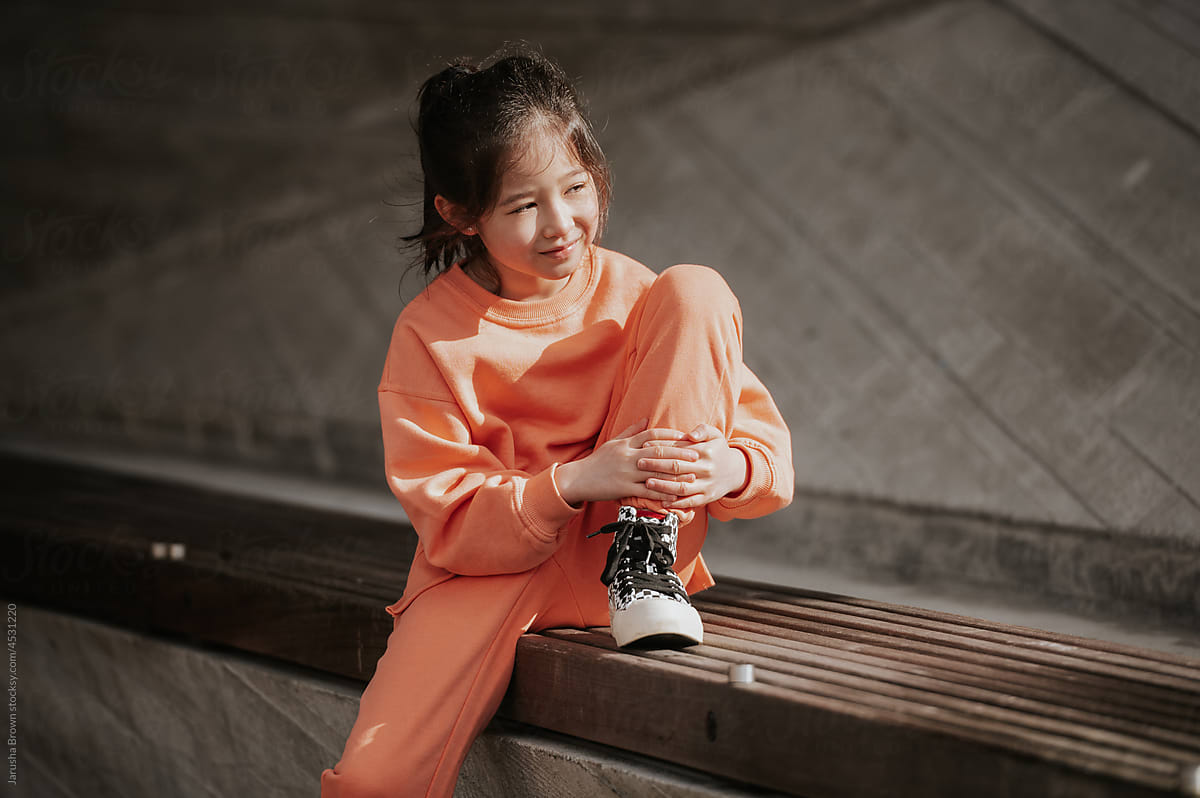 Young girl in workout clothes sits near a concrete wall.