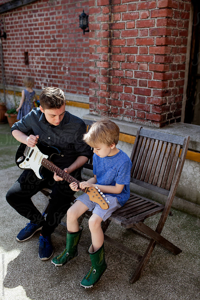 Teen boy teaches little brother to play guitar.