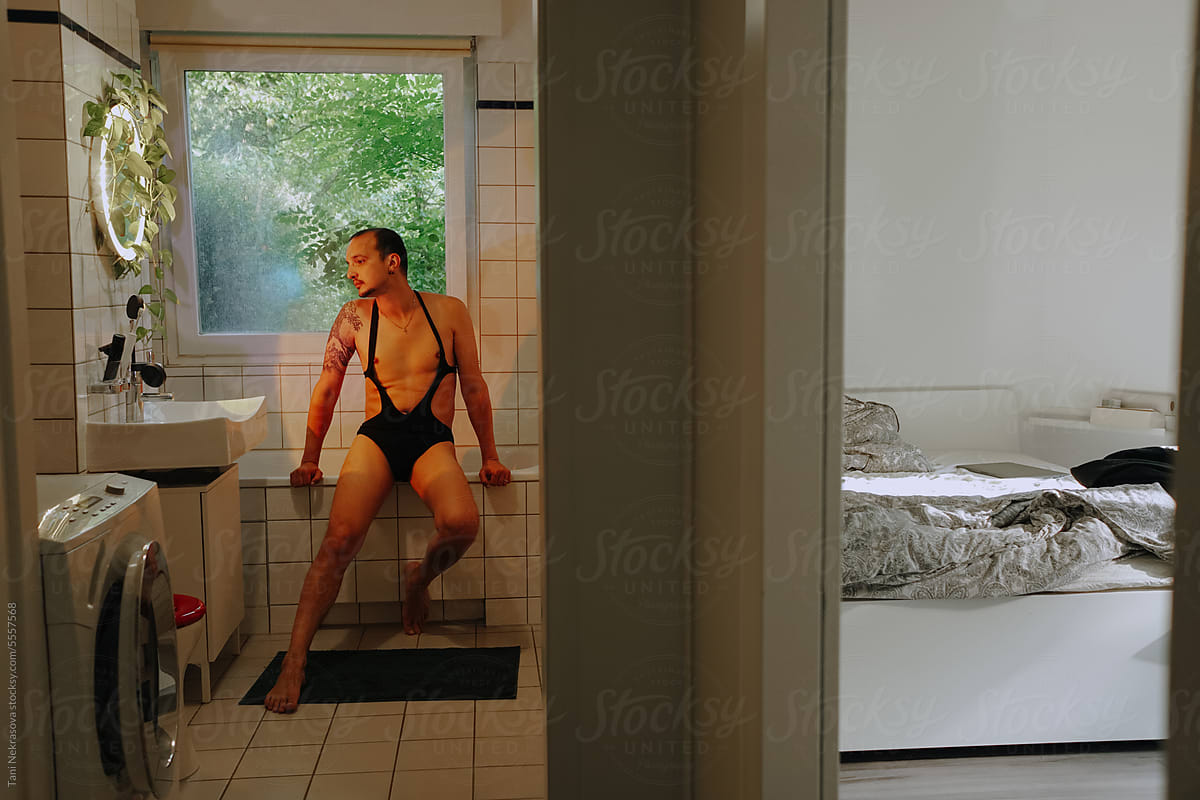 A man in a  swimsuit in his bathroom with colored lights and a window
