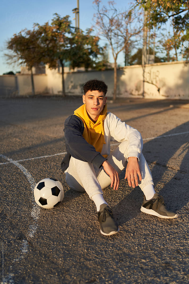 Relaxed man with soccer ball sitting on sports ground
