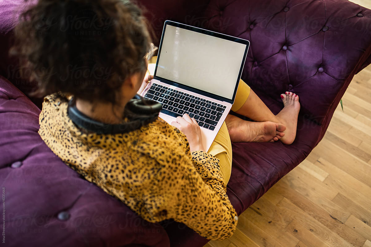 Woman works on golden laptop on purple sofa