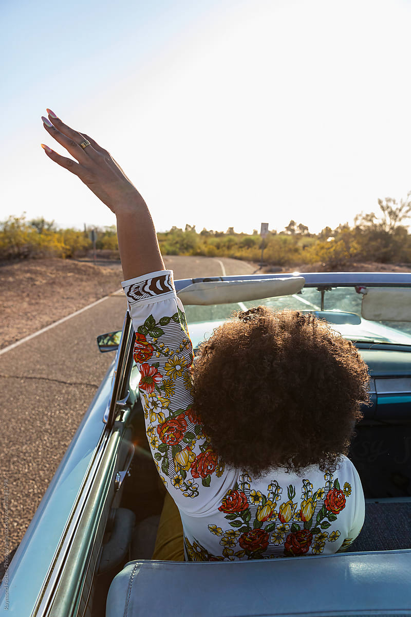 Black woman with arm raised driving vintage Automobile on Desert Roadtrip