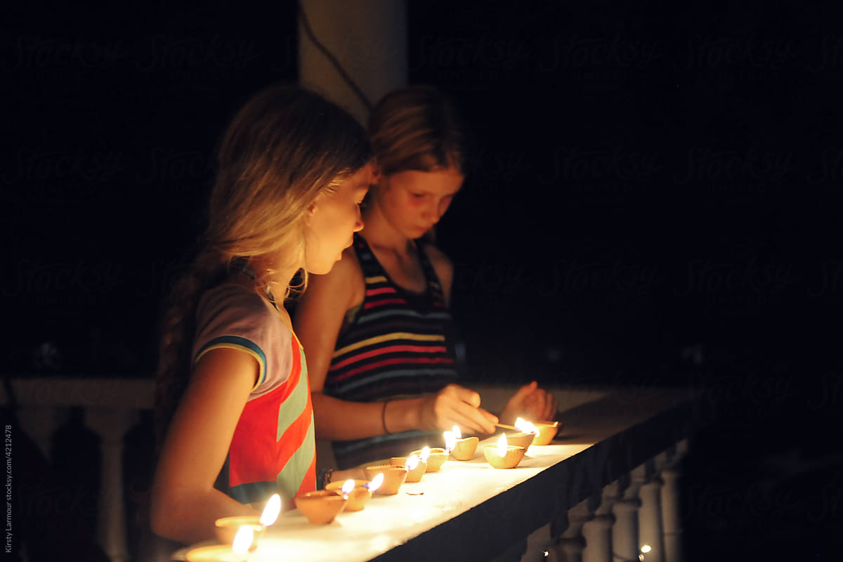 2 girls light candles for diwali on their balcony