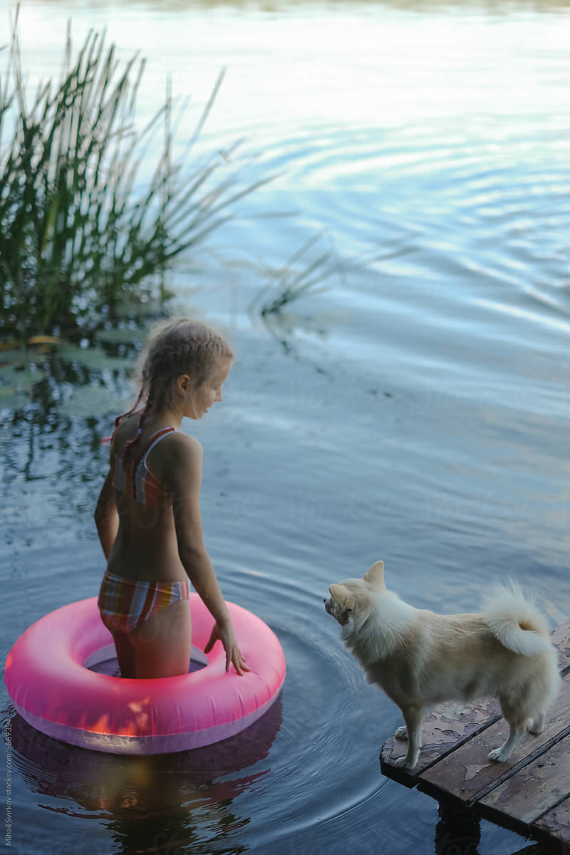 A teenage girl bathes in a lake with a pink circle and a dog.