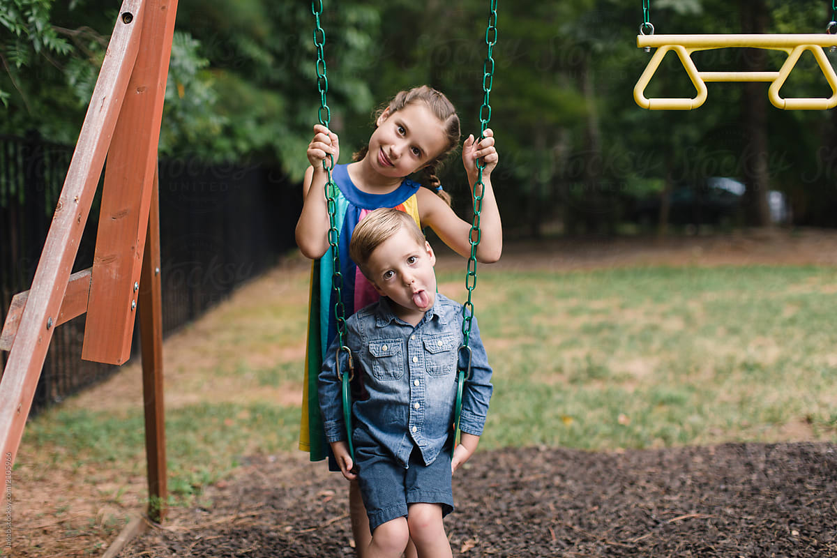 Big Sister Standing Behind Younger Brother Who Is Sitting On A Swing By Stocksy Contributor 9951